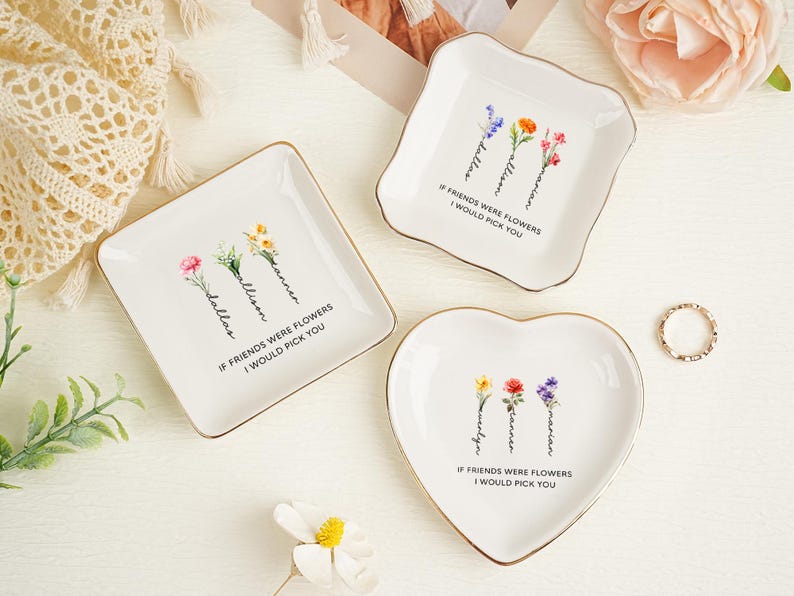 May include: Three white ceramic trinket dishes with gold-toned rims in square, scalloped, and heart shapes. Each dish features watercolor-style floral illustrations, personalized names, and the printed text: IF FRIENDS WERE FLOWERS I WOULD PICK YOU.