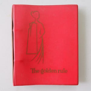 May include: A red book featuring a gold illustration of a person and the text "The golden rule." The book's cover shows signs of wear.