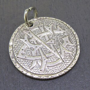 May include: Silver charm with a detailed design of a stylized letter 'X' with a loop at the top for attaching to a chain or bracelet.