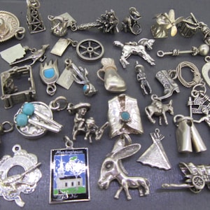 Puede incluir: Una colección de dijes plateados, que incluyen un sombrero, un vaquero, una herradura y una carreta cubierta. Otros dijes incluyen una iglesia, un burro y un tipi nativo americano. Los dijes son probablemente para una pulsera o un collar.