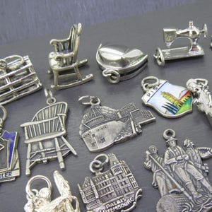 Pu&ograve; includere: Una collezione di ciondoli argentati, tra cui una sedia a dondolo, una macchina da cucire, un medaglione a forma di cuore e una sedia in miniatura. Altri ciondoli raffigurano una nave, un edificio e un'artista di bandiera. I ciondoli sono su una superficie grigio scuro.