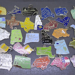 May include: A collection of vintage state-shaped charms, each with a different color and design. The charms feature the names of states and their capital cities. The charms are made of metal and have a loop for attaching to a chain or bracelet.