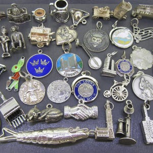 May include: A collection of vintage silver charms, including miniature trains, buildings, and figures. Some charms feature enamel details in blue, green, and red. The charms are of various shapes and sizes, suitable for jewelry making or collecting.