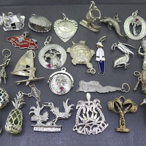 May include: A collection of 20 silver charm pendants featuring various designs, including a pineapple, a sailboat, a turtle, a pelican, a palm tree, a seashell, and a  'New Providence' charm.
