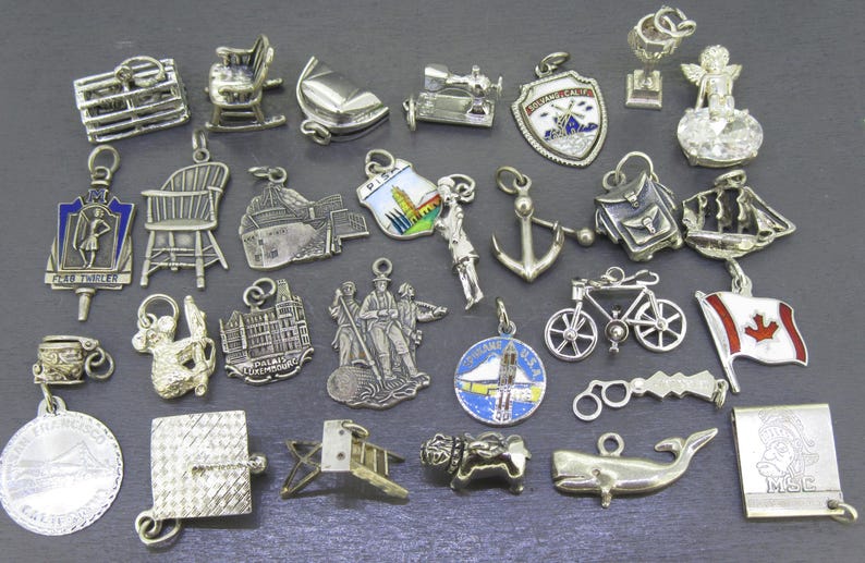 Pu&ograve; includere: Una collezione di ciondoli argentati in varie forme, tra cui sedie, una sedia a dondolo, una barca a vela, una macchina da cucire, uno scudo, un angelo, uno zaino, un'ancora, una bicicletta, una bandiera canadese e altro.