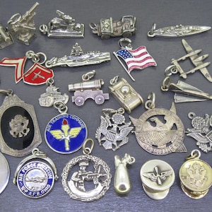 Peut inclure: Une collection de breloques et pendentifs vintage sur le thème militaire, en argent et or. L'assortiment comprend des chars miniatures, des avions, des drapeaux, des médailles et des insignes militaires, pour la création de bijoux ou la collection.