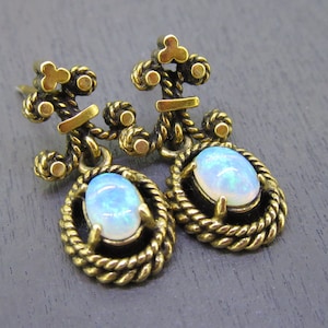 May include: A pair of gold-toned earrings with opal stones. The earrings feature a detailed design with a rope-like pattern and a small, ornate top.