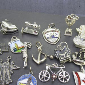 Pu&ograve; includere: Una collezione di ciondoli argentati, tra cui una sedia a dondolo, una macchina da cucire, uno scudo con un disegno di mulino a vento, un trofeo, un angelo, una nave, una bicicletta e una bandiera canadese. I ciondoli sono dettagliati e vari.