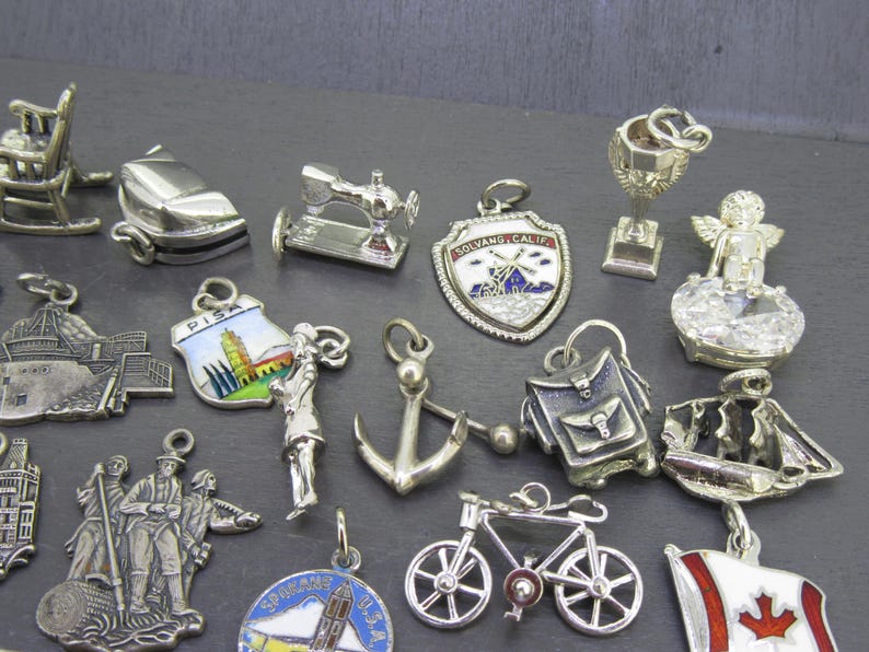 Pu&ograve; includere: Una collezione di ciondoli argentati, tra cui una sedia a dondolo, una macchina da cucire, uno scudo con un disegno di mulino a vento, un trofeo, un angelo, una nave, una bicicletta e una bandiera canadese. I ciondoli sono dettagliati e vari.