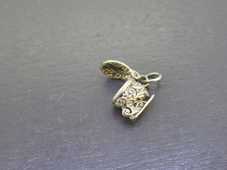 Pu&ograve; includere: Un piccolo ciondolo color argento con un design ornato. Il ciondolo sembra essere una tazza e un piattino in miniatura, con dettagli a volute. Il ciondolo &egrave; probabilmente in metallo ed &egrave; sospeso da un piccolo anello.