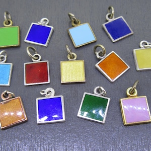 May include: A collection of square pendants with colorful enamel in various shades, including green, blue, red, and yellow. Each pendant has a silver or gold-toned frame and a small loop for attaching to a chain or bracelet.