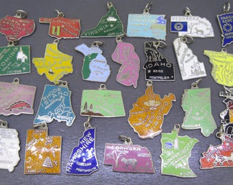 Könnte beinhalten: Eine Sammlung von Vintage-Metallanhängern in Form von US-Bundesstaaten. Jeder Anhänger hat eine andere Farbe und ein anderes Design, mit Staatsnamen und Wahrzeichen. Sie haben eine silberne Schlaufe zur Befestigung. Staaten: North Carolina, Oklahoma, Wyoming.