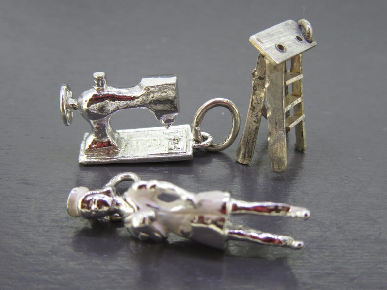 Pu&ograve; includere: Tre ciondoli d'argento: una macchina da cucire, una piccola scala e una figura sdraiata. Il ciondolo della macchina da cucire ha un design dettagliato. La scala &egrave; una versione in miniatura. La figura &egrave; sdraiata con le braccia e le gambe distese.