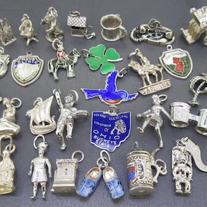 Peut inclure: Collection de breloques en argent vintage, dont un trèfle à quatre feuilles, un oiseau bleu, un écusson avec le logo de l'Ohio State et diverses autres figurines miniatures. Les breloques sont de tailles et de formes variées, avec des détails complexes.