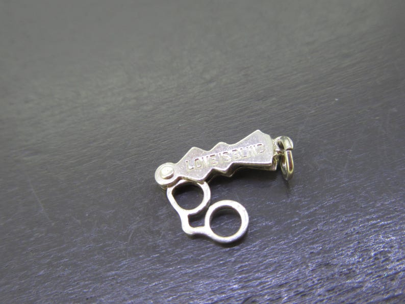 Pu&ograve; includere: Una chiusura per gioielli color argento con la scritta incisa "LOVE'S BLIND". La chiusura presenta un design unico a forma di montagna e due anelli circolari. &Egrave; progettata per fissare i gioielli.