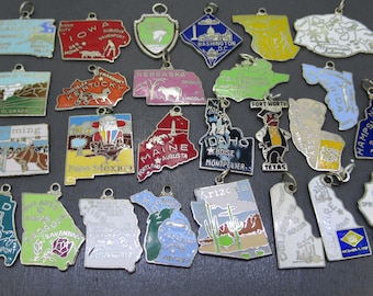 May include: A collection of twenty-eight metal state-shaped charms featuring colorful enamel designs, geographic outlines, and printed text identifying various U.S. states and cities, each equipped with a small silver-toned jump ring for attachment.