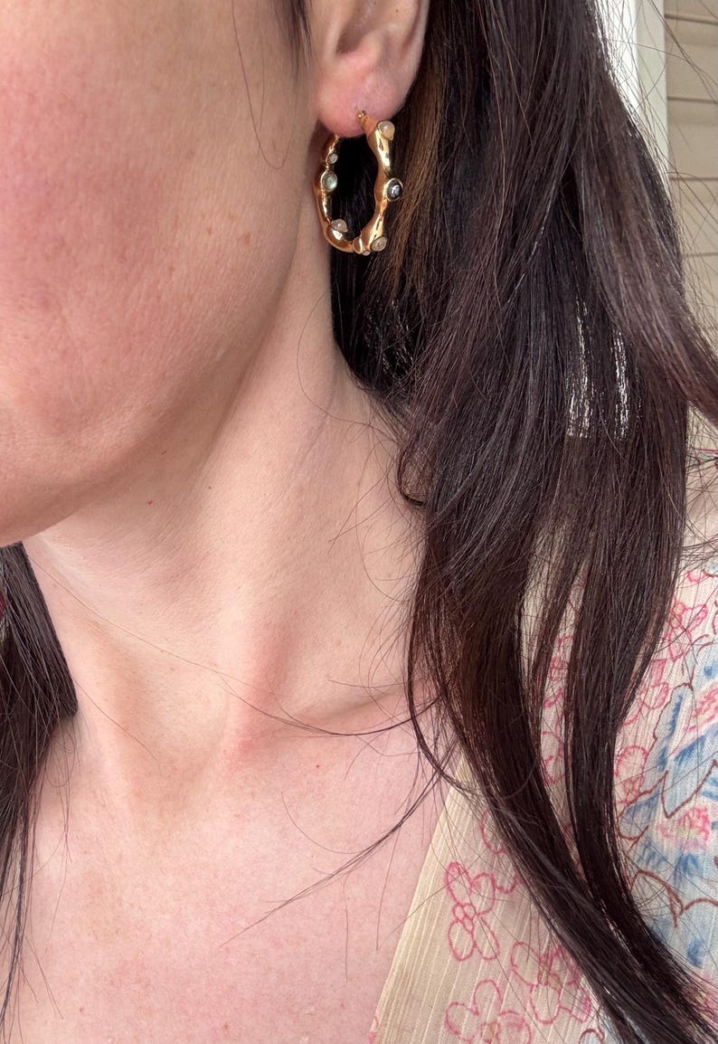 May include: Gold-toned hoop earrings with an organic, textured design. The earrings are adorned with small, clear and dark-colored stones. The jewelry is a stylish accessory, suitable for various occasions.