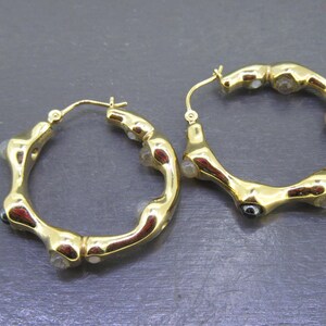 May include: A pair of gold-tone hoop earrings. The earrings have a unique, textured design with small, clear and dark accents. The hoops are round and have a lever back closure.