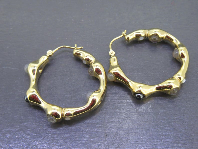 May include: A pair of gold-tone hoop earrings. The earrings have a unique, textured design with small, clear and dark accents. The hoops are round and have a lever back closure.
