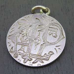 Può includere: Ciondolo in argento con un designo inciso dettagliato di una croce e la lettera "F".