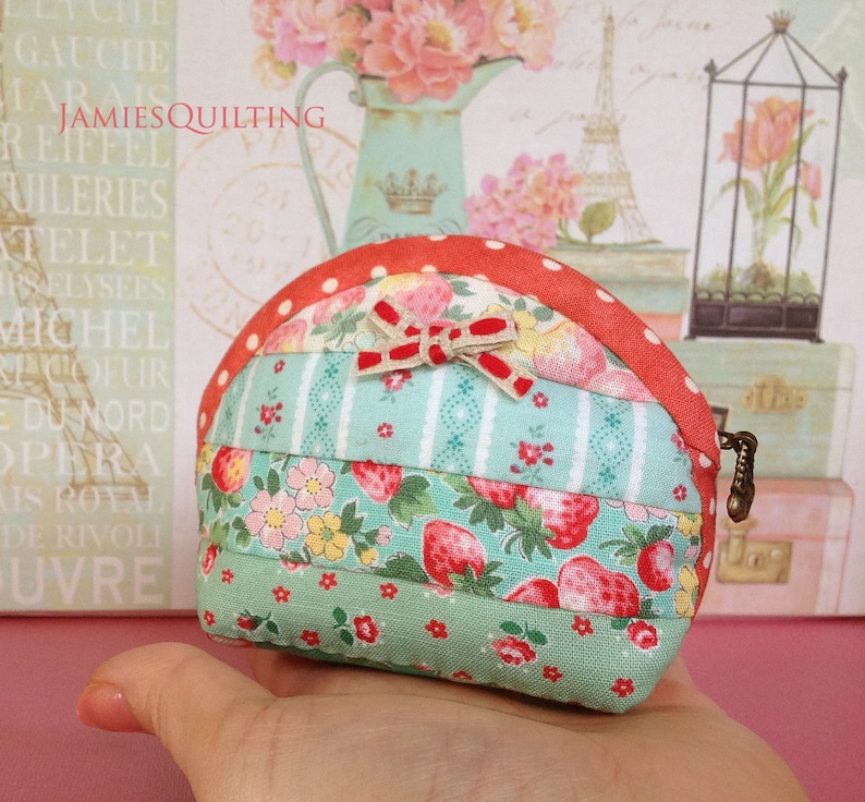 May include: A small, red, white, and green patchwork fabric coin purse with a bow and a zipper closure.