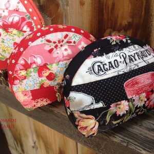 Może przedstawiać: Trzy ręcznie robione portmonetki z tkaniny w r&oacute;żnych wzorach. Pierwsza portmonetka jest czerwona i r&oacute;żowa z truskawkami i kwiatami. Druga portmonetka jest czerwona i biała z truskawkami i kwiatami. Trzecia portmonetka jest czarna w białe kropki i z kwiatowym wzorem. Portmonetka ma napis "Cacao-Payraud".