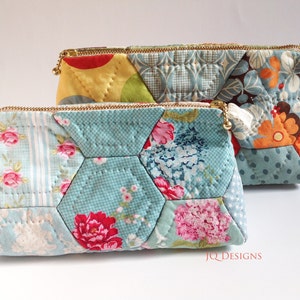 May include: Two quilted fabric zippered pouches with a patchwork design. The top pouch is blue, orange, and green with a floral pattern. The bottom pouch is blue and pink with a floral pattern. Both pouches have gold zippers and are made by JQ Designs.