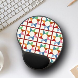 May include: Ergonomic mouse pad with a colorful geometric pattern featuring stars and triangles in red, blue, green, orange, and pink. The pad has a black wrist rest for comfort and support. Ideal for computer users.