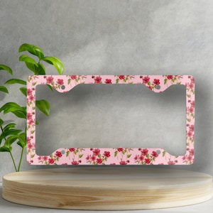 Op de afbeelding: Een roze kentekenplaathouder met een bloemenpatroon met rode bloemen en groene bladeren.
