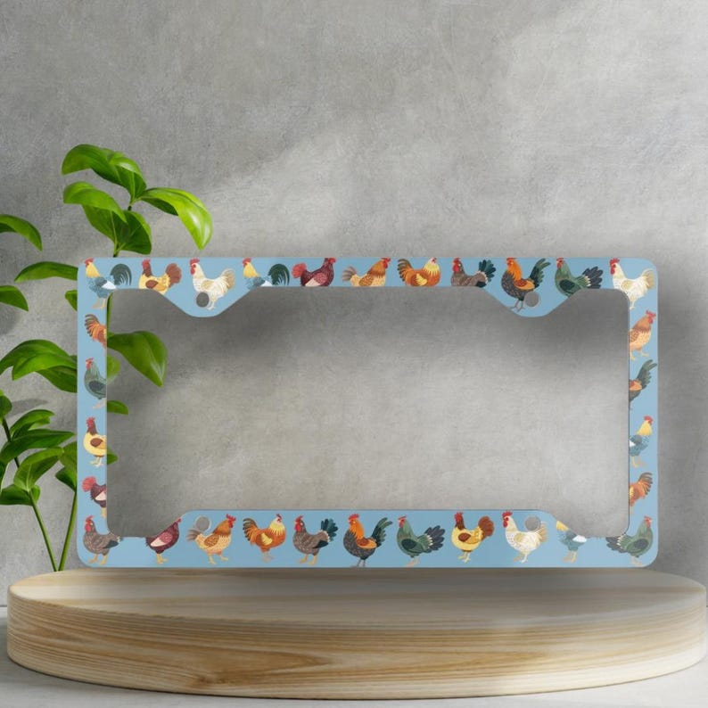 Pode incluir: Um porta-placas azul com uma borda de galos coloridos. O porta-placas &eacute; feito de metal e tem um inserto de pl&aacute;stico transparente para a placa.