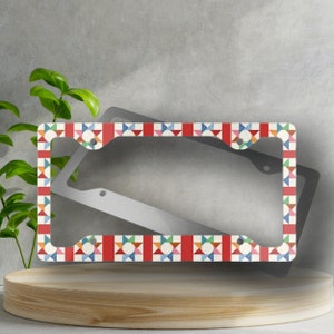 May include: A metal license plate frame with a colorful geometric pattern. The frame is red, white, blue, green, orange, and yellow. The pattern is made up of small squares and triangles.