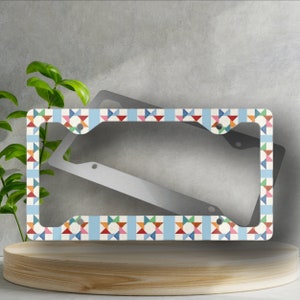 May include: A blue and white license plate frame with a colorful geometric pattern. The frame is made of metal and has two holes for attaching it to a license plate.