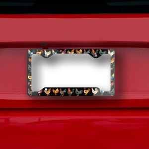 May include: License plate frame with a black border featuring a repeating pattern of colorful rooster illustrations. The frame is set against a red background, creating a vibrant contrast. The frame is designed to hold a standard license plate.