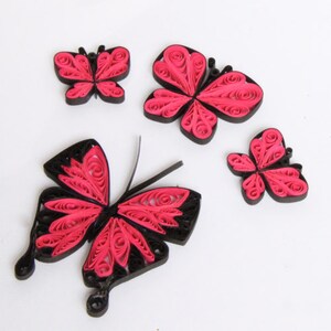 May include: Four paper butterflies with black and pink curled paper designs. The butterflies are arranged on a white surface.
