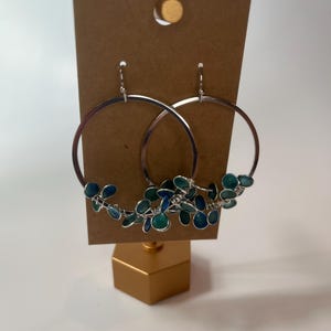 May include: Silver hoop earrings with a cluster of blue and green enamel leaves dangling from the bottom.