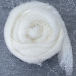 May include: A close-up of a white, fluffy ball of wool yarn. The yarn is rolled up in a spiral shape and has a soft, delicate texture.