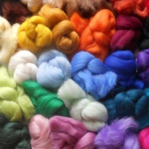May include: A collection of colourful wool roving in various shades, including blue, green, purple, pink, yellow, orange, and white. The wool is arranged in a loose pile, showing the texture and softness of the fibres.