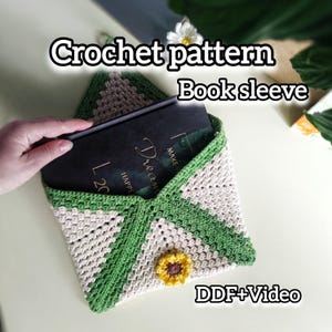 May include: A handmade crochet book sleeve in cream, green, and tan. The sleeve has a sunflower applique and a chevron pattern. The text "Crochet pattern Book sleeve" is displayed on the image.