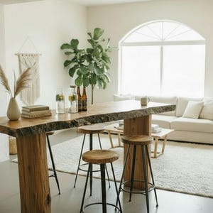 Puede incluir: Una mesa de bar rústica de madera con borde natural, sostenida por una base de madera gruesa. Tres taburetes de madera y metal negro están frente a la mesa. Un sofá y una alfombra blancos están en el fondo.