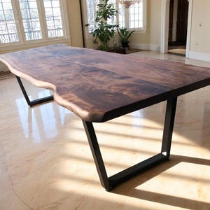 May include: A large, live edge wooden table with a dark brown finish. The table is supported by black metal legs. The table's dimensions are approximately 244 cm long and 102 cm wide.
