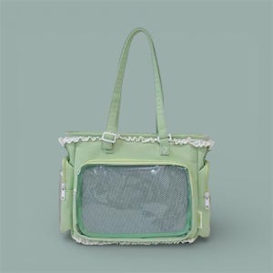 Peut inclure: Un sac fourre-tout vert clair avec une poche en filet rectangulaire et deux poches latérales. Le sac a une bordure en dentelle blanche et deux poignées. Le sac est fait d'un matériau doux et possède une fenêtre en plastique transparent.