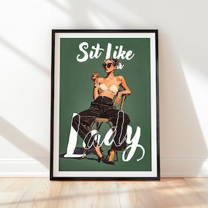 May include: Framed art print with a retro illustration of a woman seated in a chair, holding a cocktail. The artwork has a green background with the words "Sit like a Lady" in white script. The woman wears sunglasses and a bra.