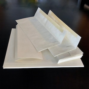 May include: A stack of white envelopes with a gummed flap and a yellow adhesive strip. The envelopes are arranged in a pyramid shape.