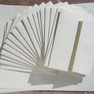 May include: A stack of white envelopes, fanned out in a semi-circle, with the top envelope folded in half. The envelopes are all the same size and are made of a smooth, white paper.
