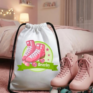 Könnte beinhalten: Ein weißer Rucksack mit Kordelzug, der eine Grafik von zwei rosa Rollschuhen auf einem hellgrünen kreisförmigen Hintergrund mit kleinen rosa Sternen zeigt. Der Name Beverley ist in Weiß auf einem grünen Banner mittig aufgedruckt.