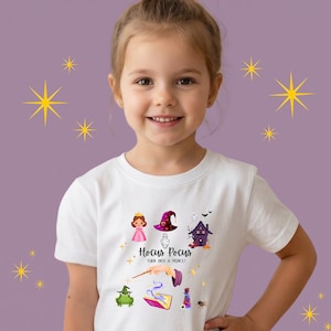 Puede incluir: Una camiseta blanca de manga corta con un estampado gráfico colorido de una princesa, un sombrero de bruja, una casa encantada, una rana, un libro de hechizos y pociones. El texto dice Hocus Pocus TURN INTO A PRINCE! con una varita.