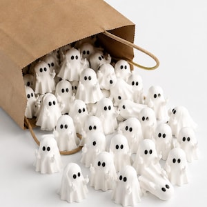 May include: A brown paper bag spilling out numerous small white ghost figurines. Each ghost is made of white material with two black oval eyes and features a small arm raised in a middle finger gesture, creating a repetitive and humorous display.