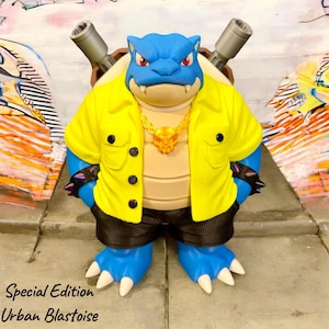 May include: A blue turtle-like figure with two grey cannons on its back, wearing a bright yellow button-down shirt, black shorts, and a gold skull necklace. The figure has red eyes and white claws. Text reads: Special Edition Urban Blastoise.