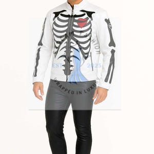 Könnte beinhalten: Weiße Lederjacke mit schwarzem Skelett-Design, einschließlich Brustkorb und Armknochen, und einem roten Herz. Die Jacke hat einen Reißverschluss und wird mit einer schwarzen Lederhose getragen. Der Text "EST 2025" ist sichtbar.