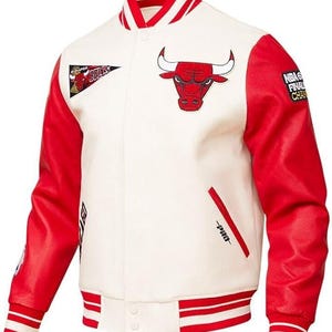 Pode incluir: Casaco universitário branco e vermelho dos Chicago Bulls. O casaco apresenta mangas vermelhas, gola, punhos e bainha listrados em vermelho e branco. O logotipo dos Bulls é exibido no peito, com patches e detalhes de texto adicionais.
